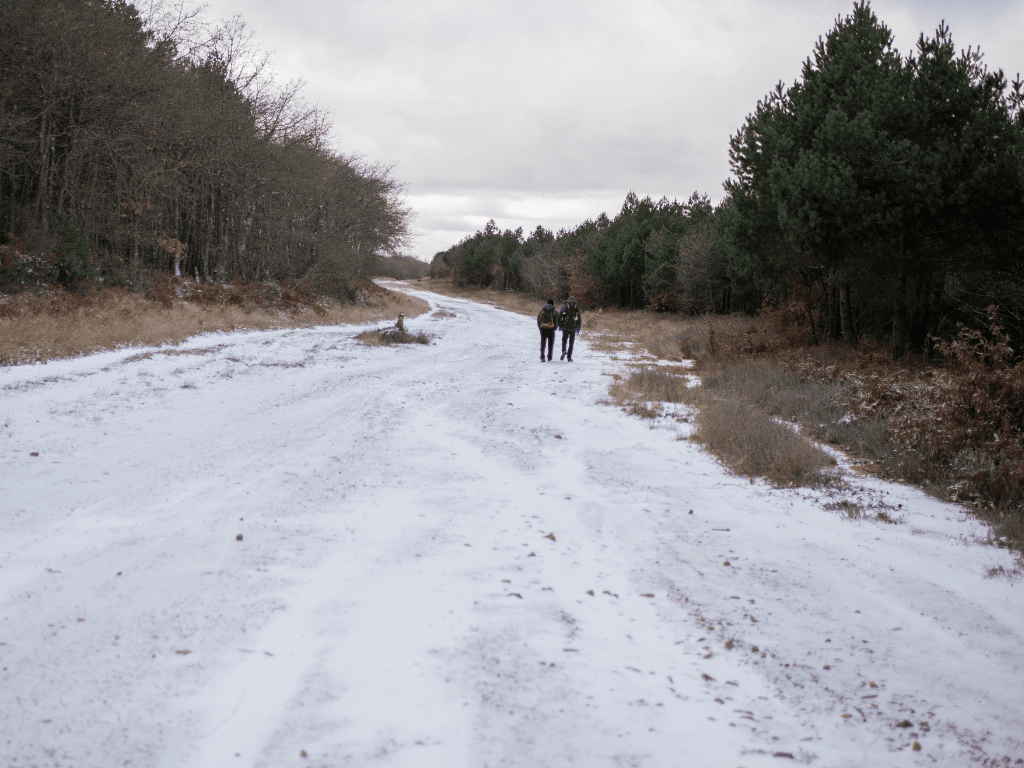 two men with backpacks walking on a secluded pathway covered in snow