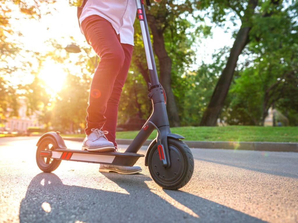 mans legs riding an electric scooter with sunshine behind