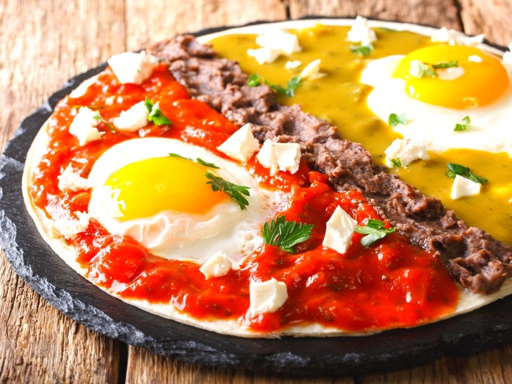a stone plate with a tortilla topped with eggs in red and green sauces, separated by a line of black beans in a Mexican dish called huevos divorciados