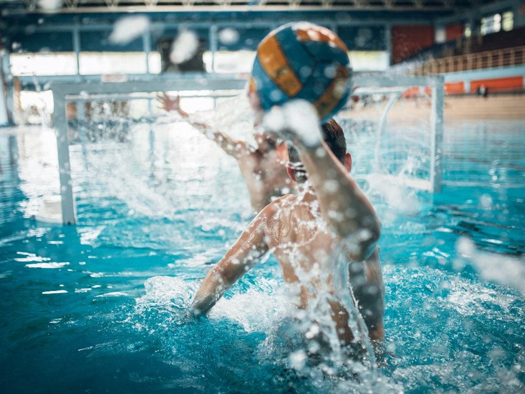 two men playing waterpolo, one throwing the ball into the net overhand