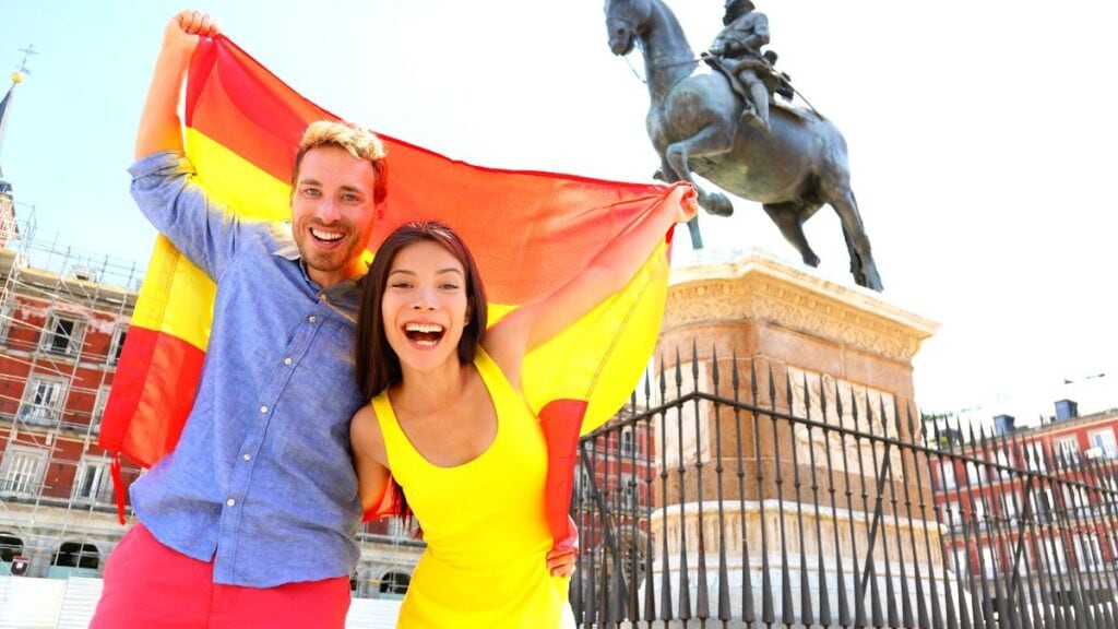 couple standing in madrid, excitedly waving spanish flag