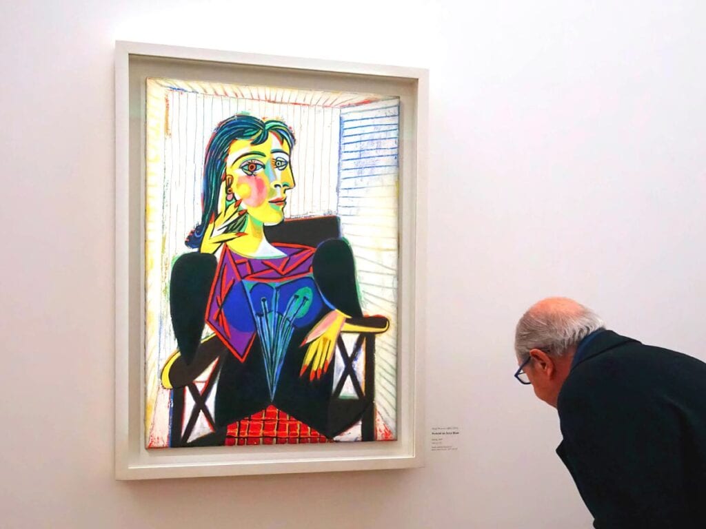 older man reading the plaque next to a Picasso portrait of a woman in a museum