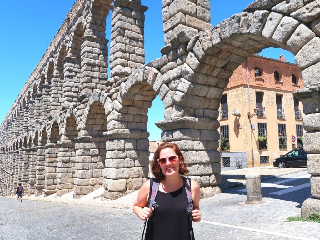 the female author of this blog standing in front of the large aqueduct in Segovia, Spain on a sunny day